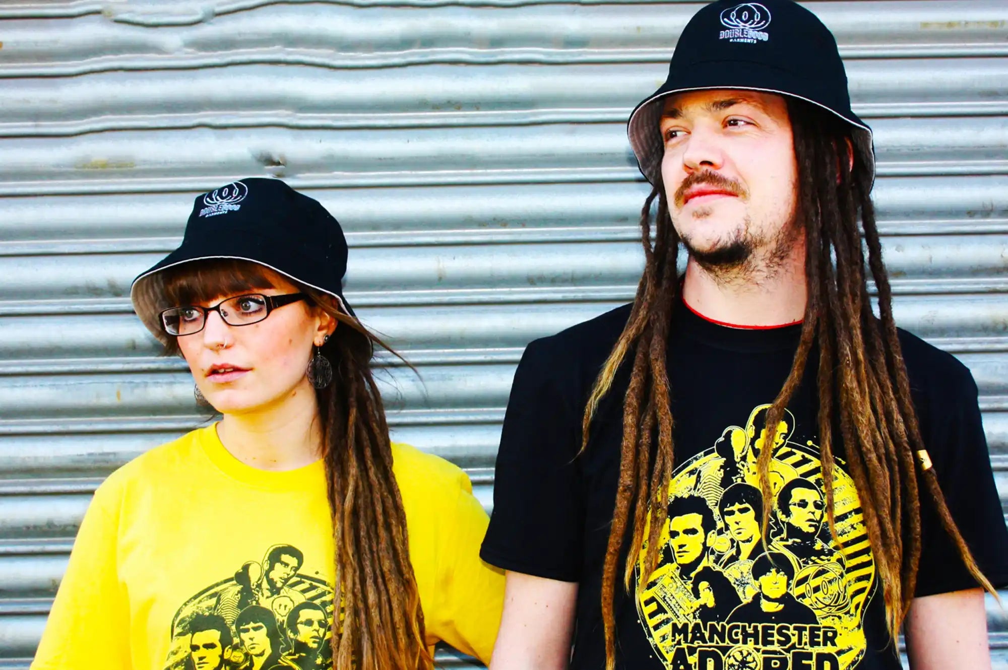 Two people with dreadlocks wearing matching hats and band t-shirts.
