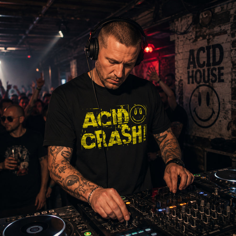 A man wearing a black graphic t-shirt with 'ACID CRASH!' in yellow text and headphones, mixing music at a DJ console in a club setting with 'ACID HOUSE' on the wall behind him.