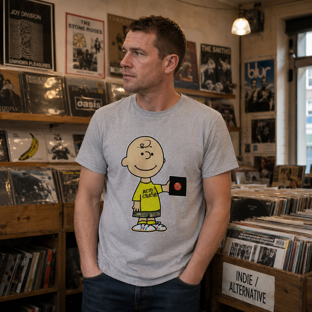 A man wearing a light gray t-shirt with a cartoon graphic of Charlie Brown and the text 'Acid Crash' standing in a record store.
