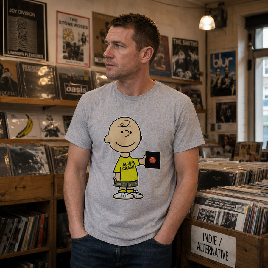 A man wearing a light gray t-shirt with a cartoon graphic of Charlie Brown and the text 'Acid Crash' standing in a record store.
